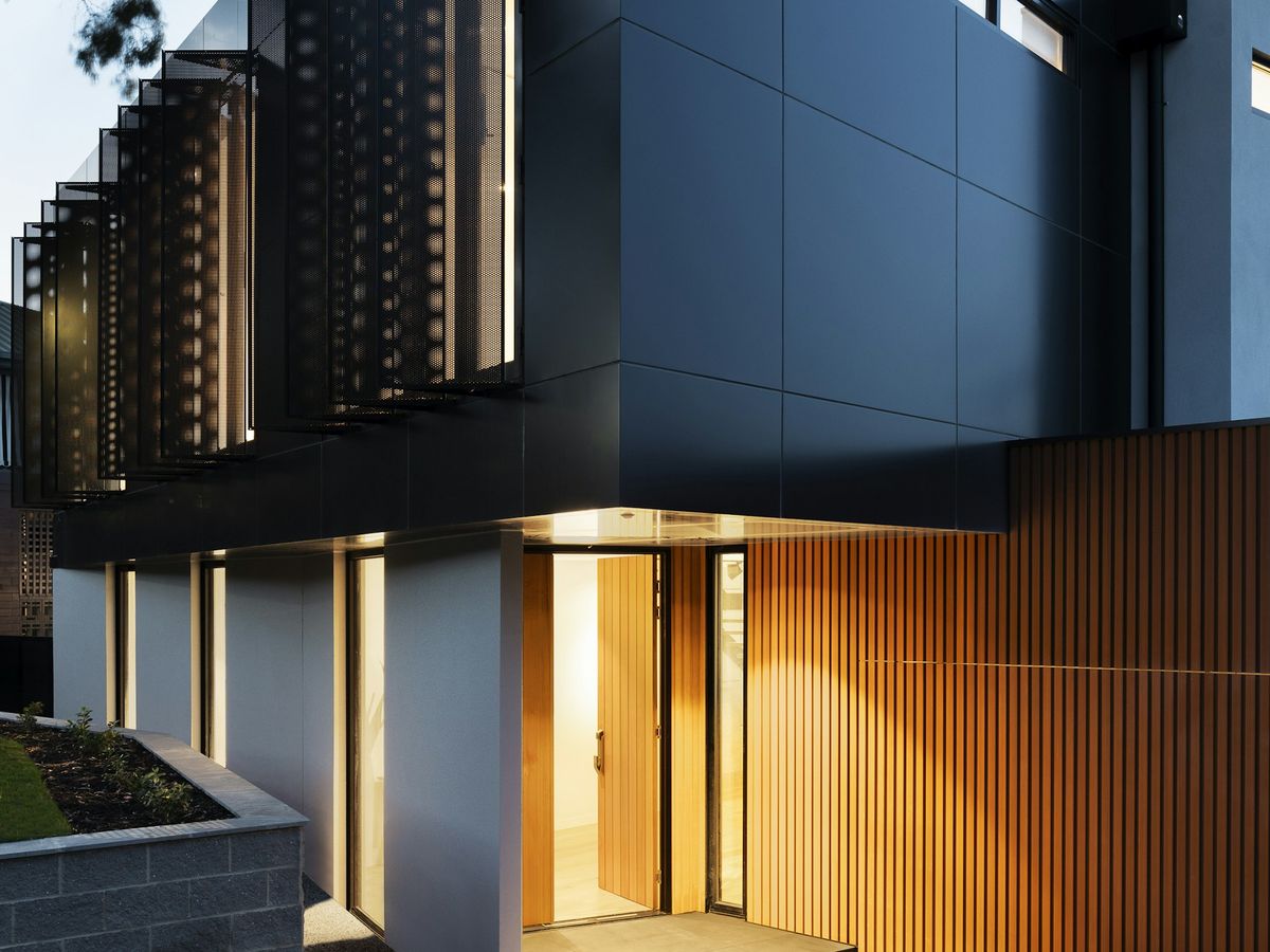 Dark-clad contemporary house at dusk with a warmly lit timber entrance
